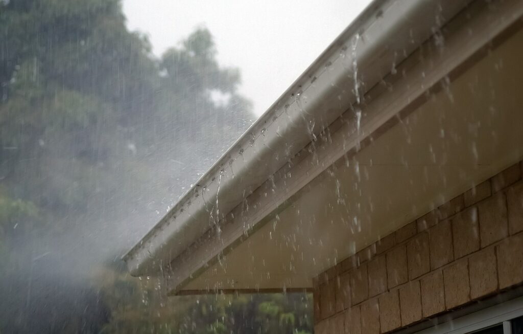 Es regnet in Strömen. An einem Hausdach ist eine Regenrinne aus Kunststoffe befestigt.