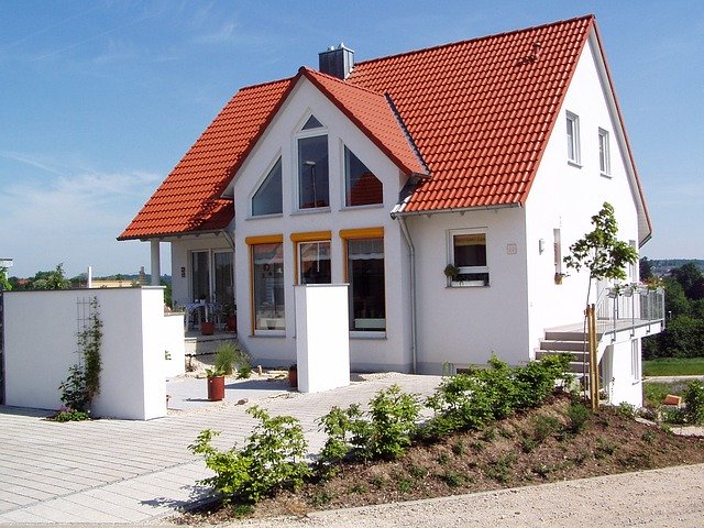 Ein neu gebautes Einfamilienhaus mit weißen Außenwänden und einem roten Dach steht auf einem Grundstück.