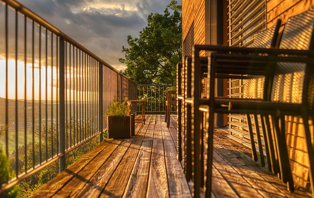 Auf einem Holzbalkon mit Metall-Geländer stehen zwei Stühle im Sonnenuntergang.