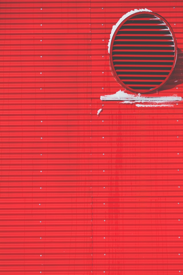 An einer roten Außenwand ist ein großer Abluftauslass zu sehen.