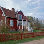 Ein rot-weißes Schwedenhaus mit einem roten Gartenzaun davor