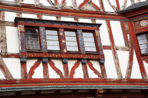 Vor dem Restaurieren: Ein altes Fachwerkhaus mit roten Balken, von denen die Farbe abblättert, und weißen Putzflächen.