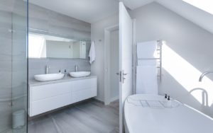 Blick in ein Badezimmer, in dem großformatige Fliesen verlegt wurden. Rechts steht die Wanne, links sind Dusche und Doppelwaschtisch.