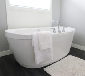 In einem fugenloses Bad steht vor einem Fenster eine weiße, freistehende Badewanne.