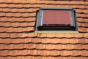 Ausschnitt eines mit roten Ziegeln gedeckten Daches, in das ein Dachliegefenster eingebaut wurde.