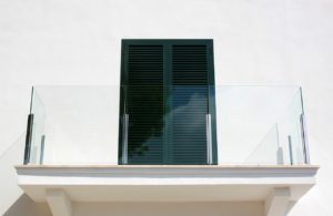 Ein nahezu unsichtbares Balkongeländer aus Glas vor einer weißen Hauswand.
