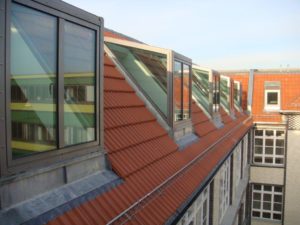 Moderne, rechteckige Dachgauben aus Glas stehen auf einem mit roten Ziegeln gedecktem Dach.