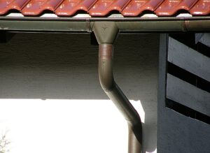 Man sieht ein klassisches Dachentwässerungssystem mit Regenrinne, Trichter und Fallrohr, angebracht an einer gewöhnlichen Hauswand.