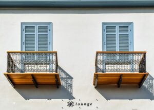 Zwei Balkons aus Holz sind nebeneinander an einer weißen Hausfassade angebracht.